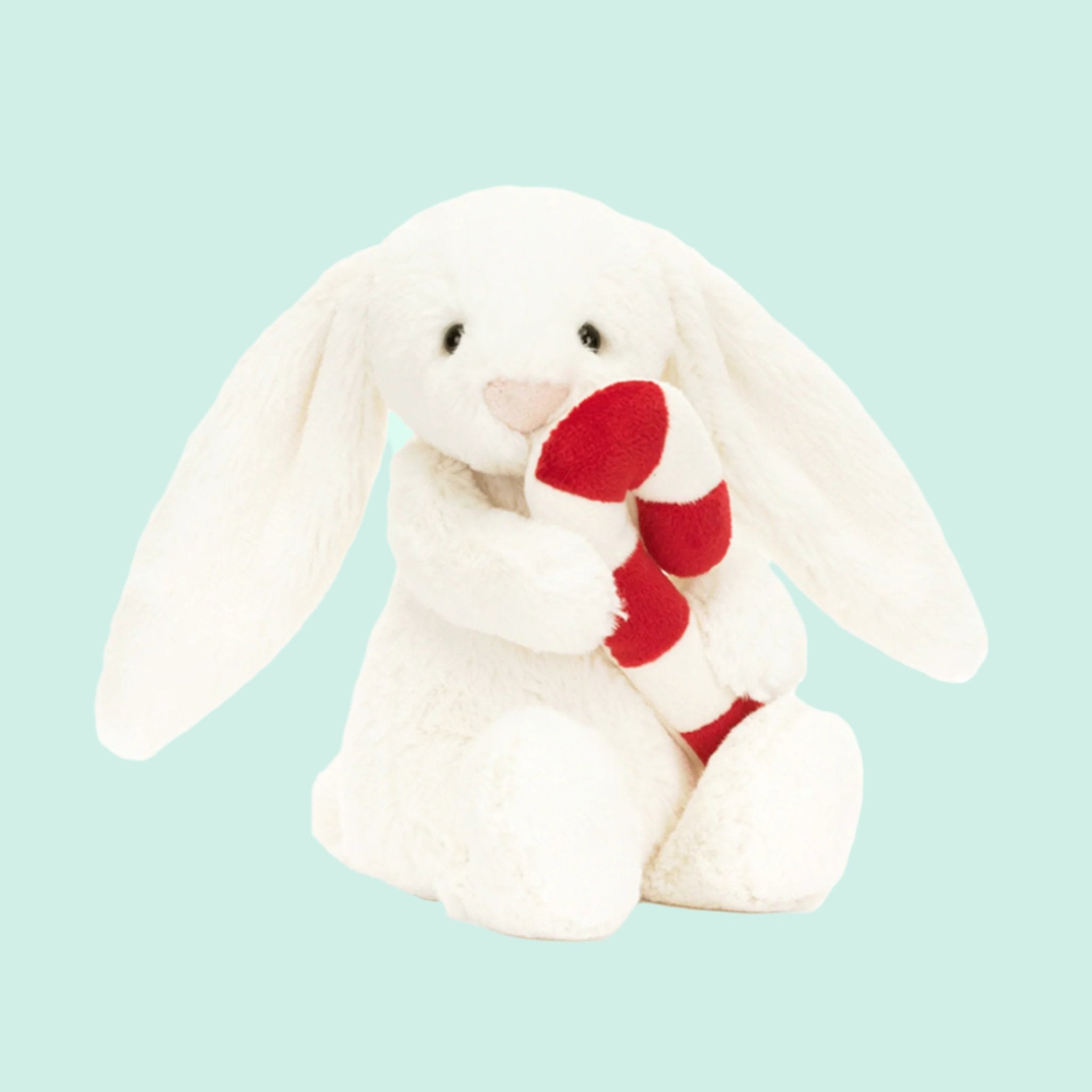 A white bunny shaped stuffed animal holding a red and white candy cane. 