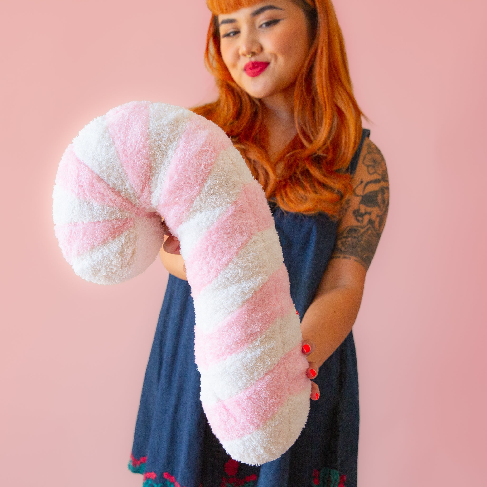 A light pink and white striped candy cane shaped pillow. 