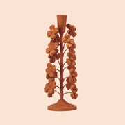 A terracotta colored cast iron taper candle holder with flower shapes on the sides. 