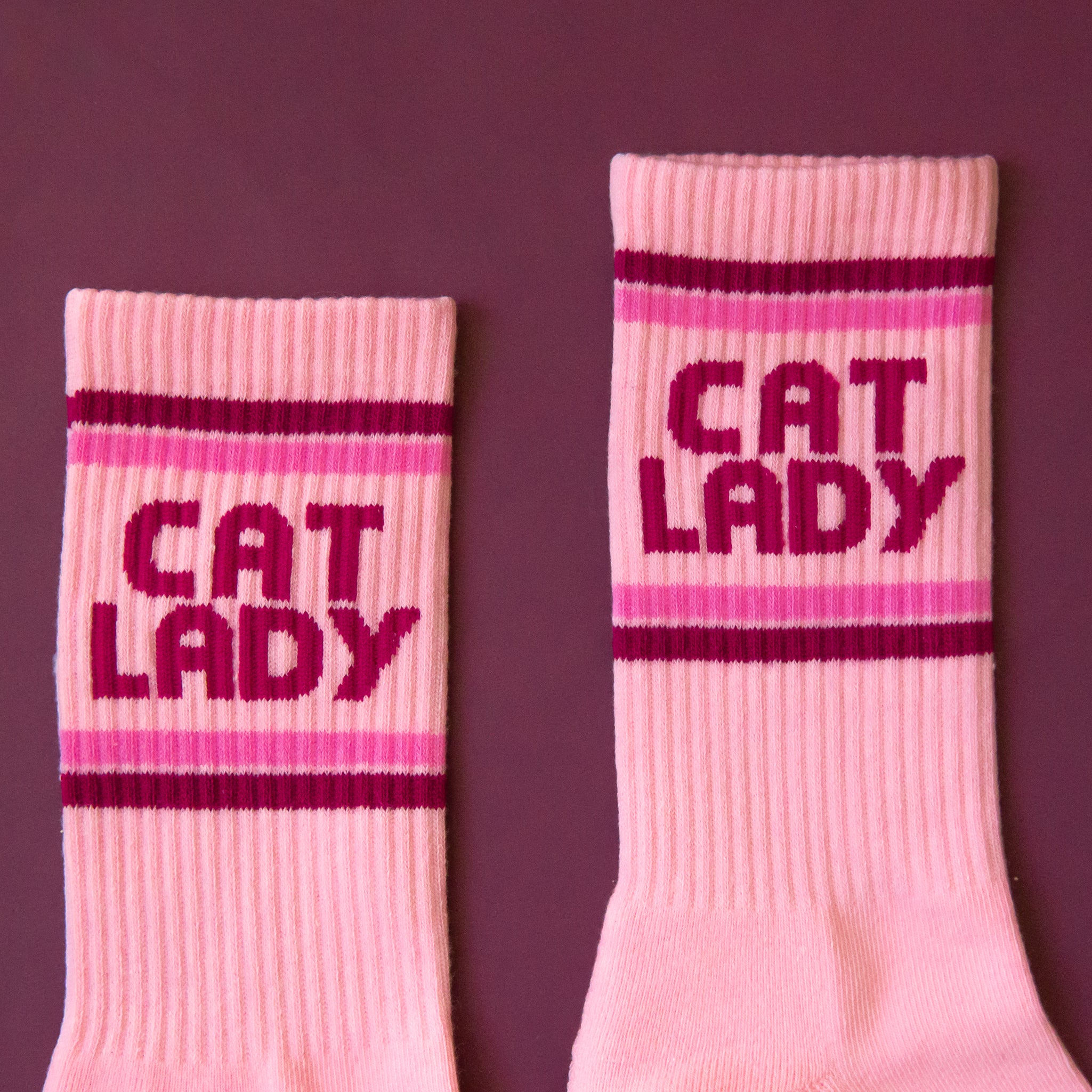 A pair of pink socks with dark pink text on the ankle of the sock that reads, &#39;Cat Lady&#39;.