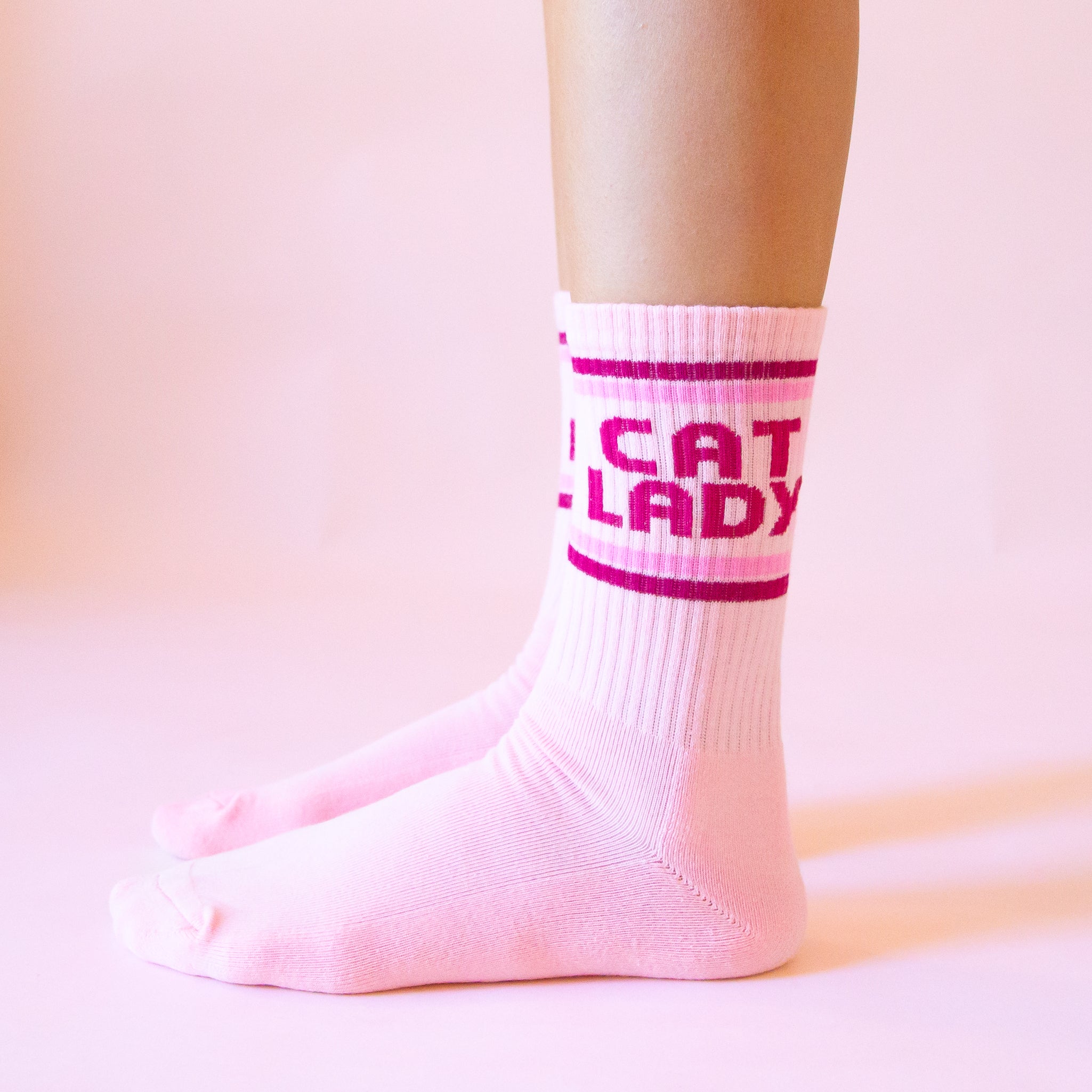 A pair of pink socks with dark pink text on the ankle of the sock that reads, &#39;Cat Lady&#39;.