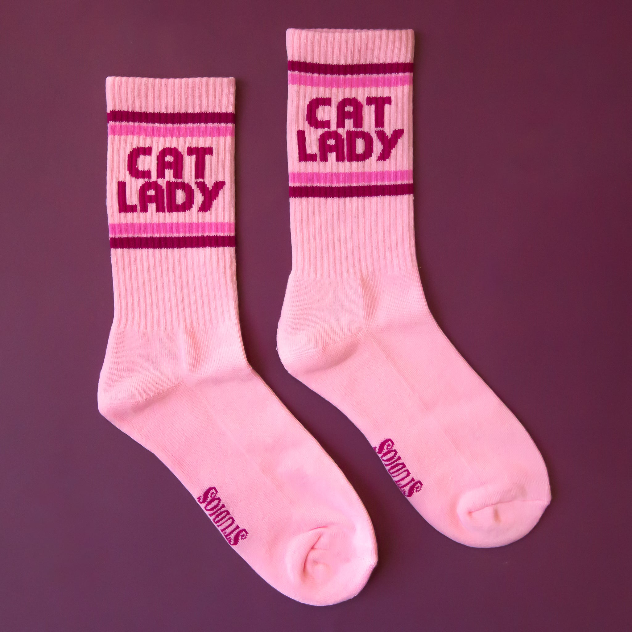 A pair of pink socks with dark pink text on the ankle of the sock that reads, 'Cat Lady'.