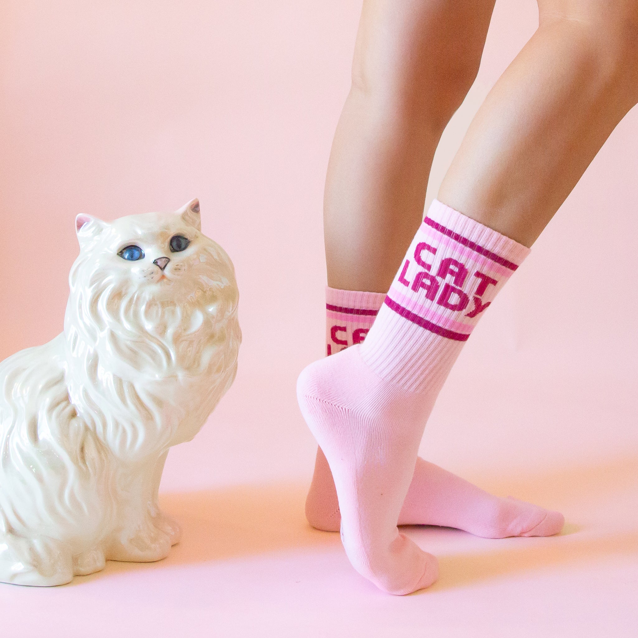 A pair of pink socks with dark pink text on the ankle of the sock that reads, 'Cat Lady'.