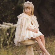 A champagne colored tulle cape with layered tiers and a neck tie with two star ribbons. 