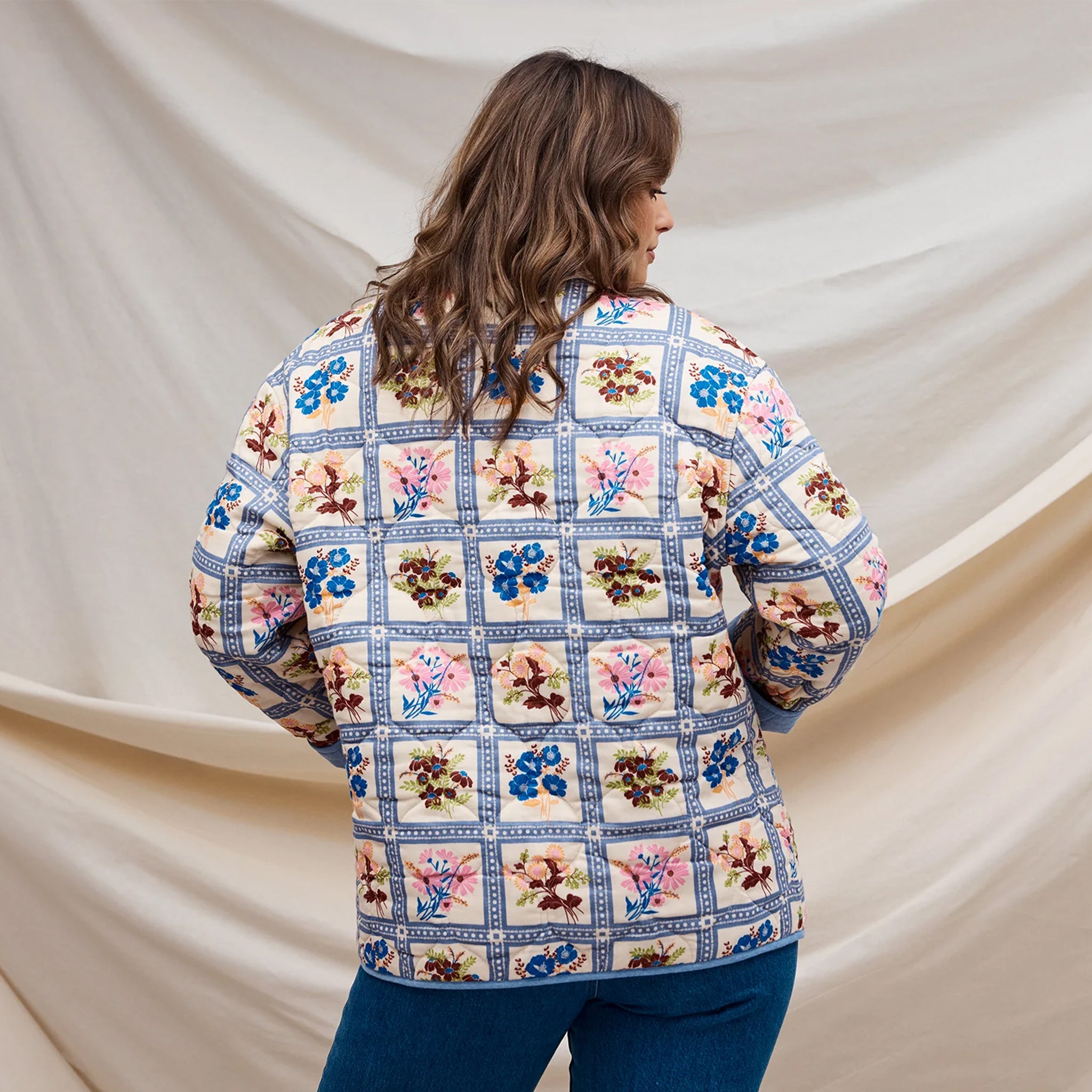 A multi colored quilted jacket with a floral print on one side and a blue solid color on the other. 