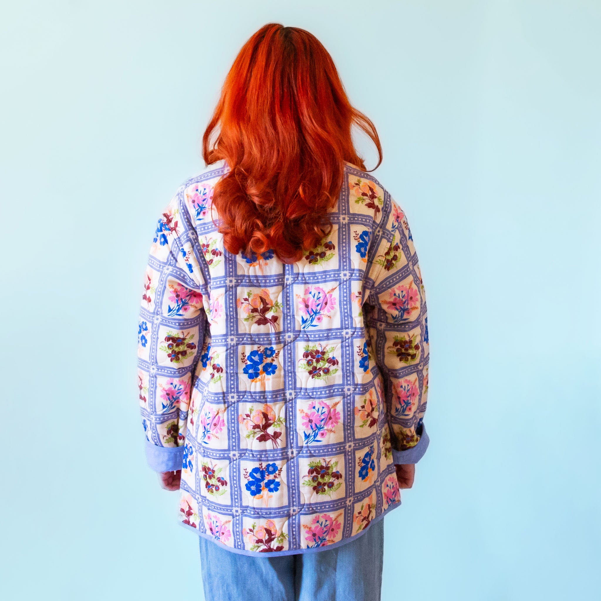 A multi colored quilted jacket with a floral print on one side and a blue solid color on the other. 