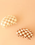 The rounded white and clear checker claw clip photographed with a brown and cream checkered claw clip with the same shape. 