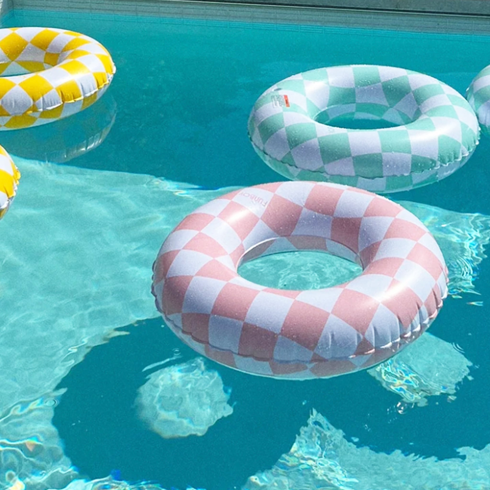 A pink and white checkered kids donut floaty in a pool with a blue and yellow option. 