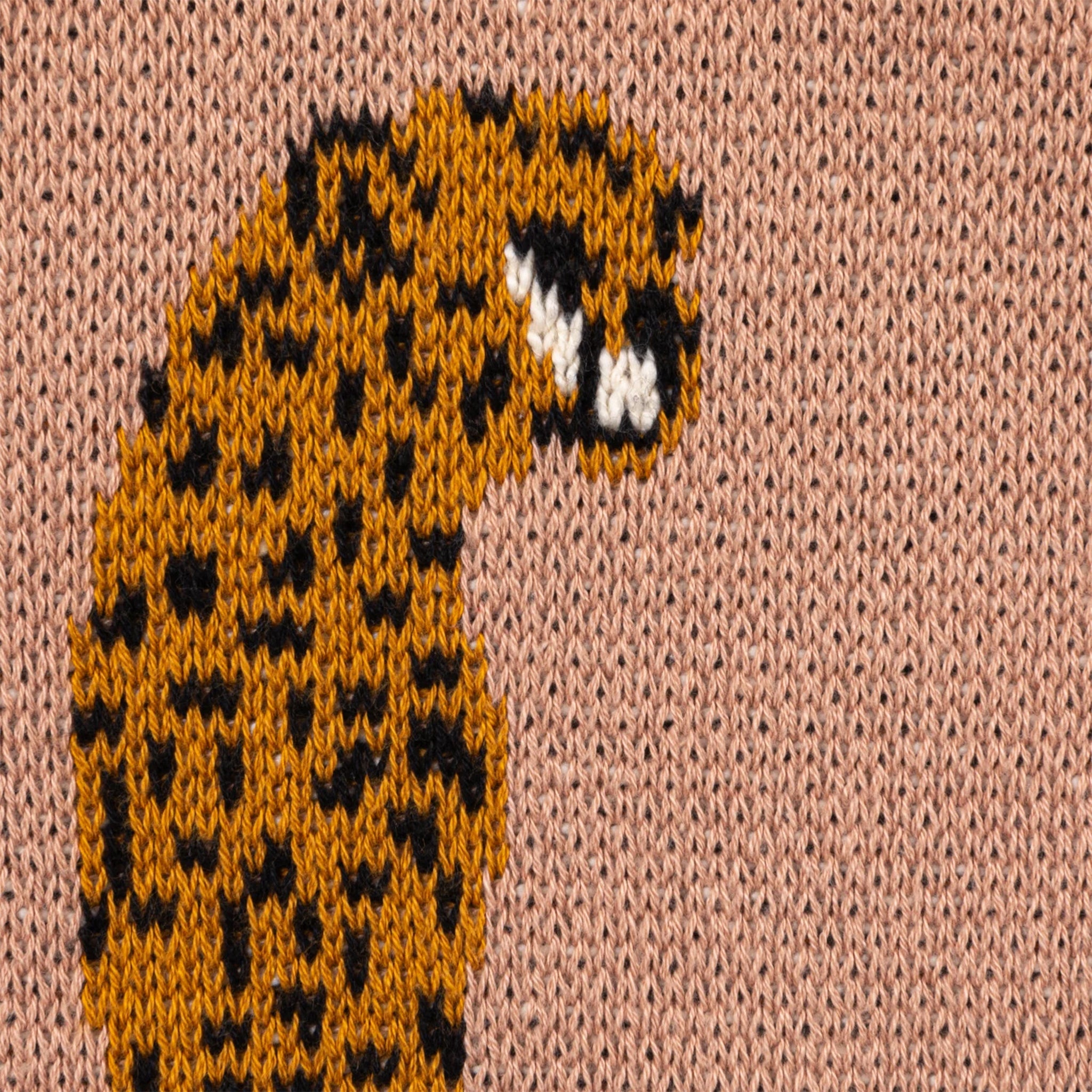 A apricot colored knitted throw blanket with a orange cheetah print. 