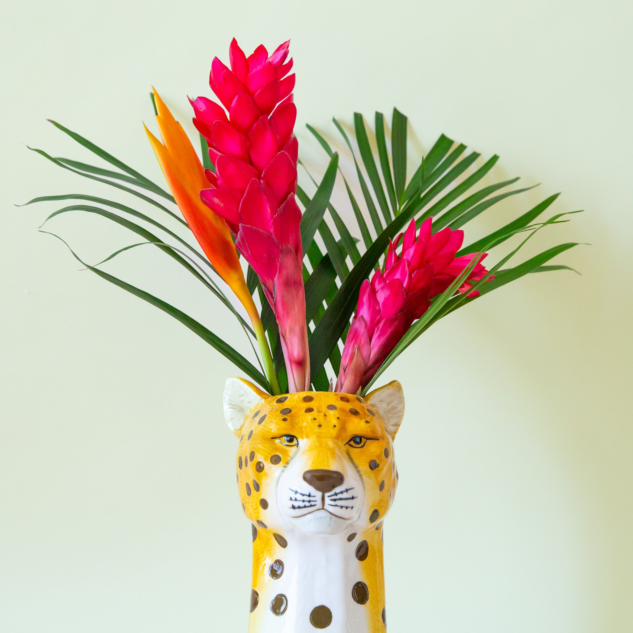 A cheetah head shaped ceramic vase with an opening at the top for an arrangement. 