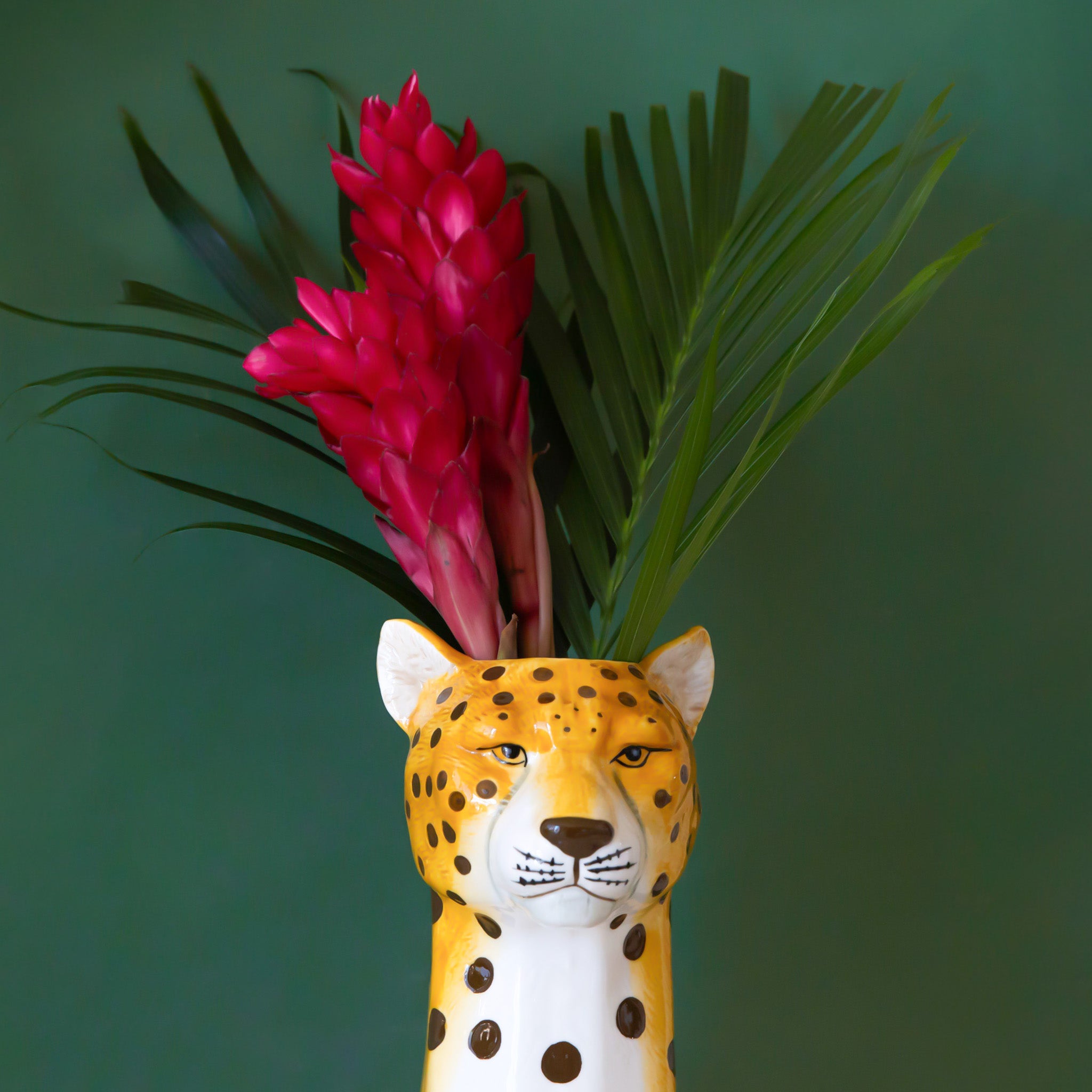 A cheetah head shaped ceramic vase with an opening at the top for an arrangement. 