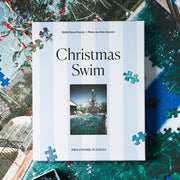 A blue and white striped puzzle box with a Slim Aarons photograph and text above that reads, 'Christmas Swim'. 