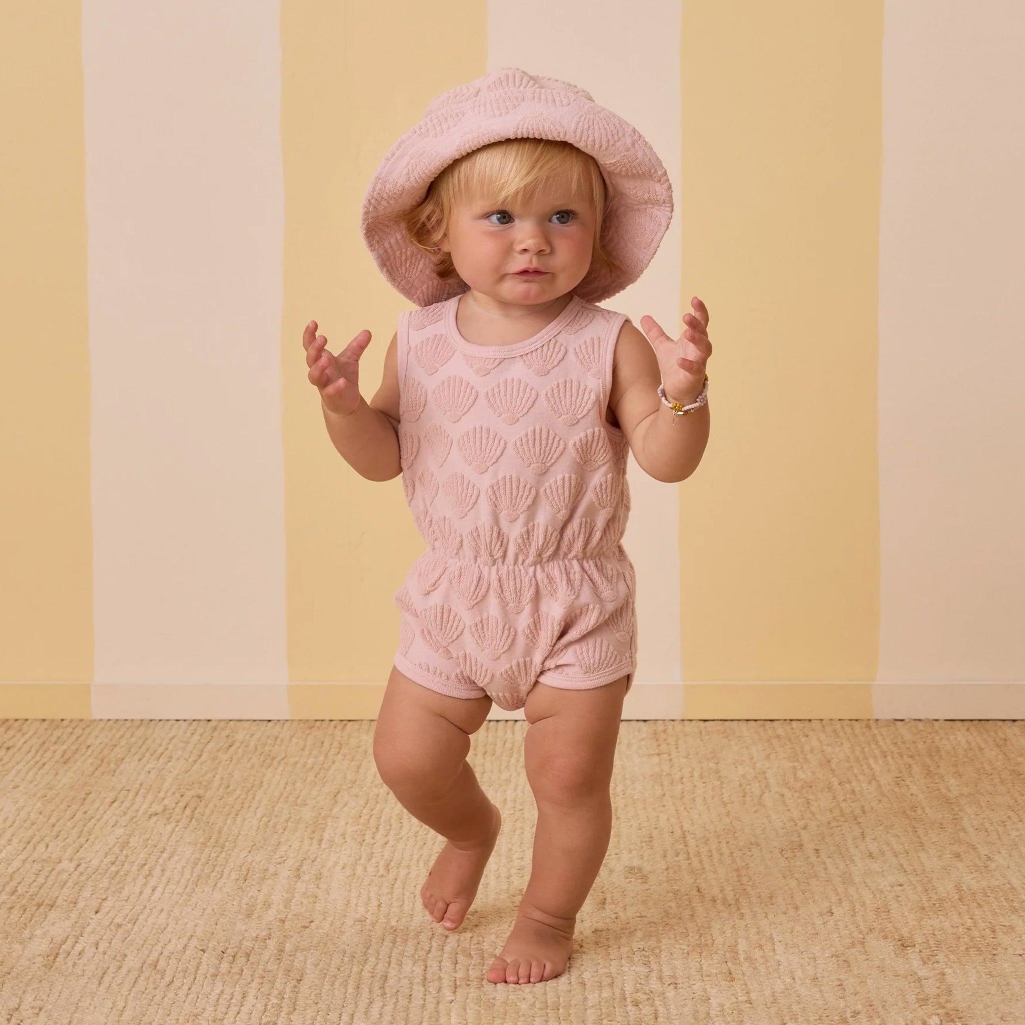 A pink kids sleeveless jumpsuit with a pink seashell pattern. 