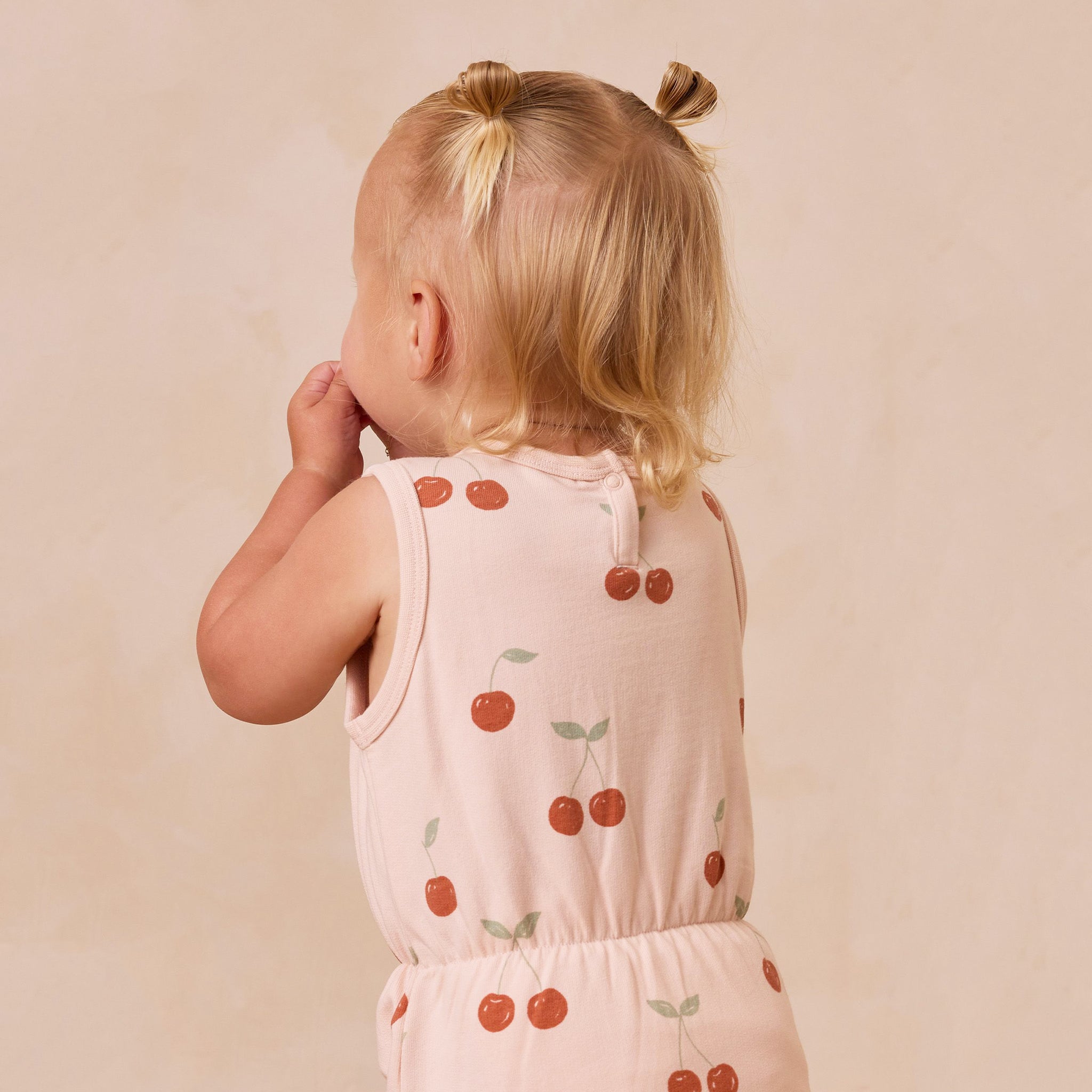 A light pink / peach colored jumpsuit with short sleeves and a cherry print. 