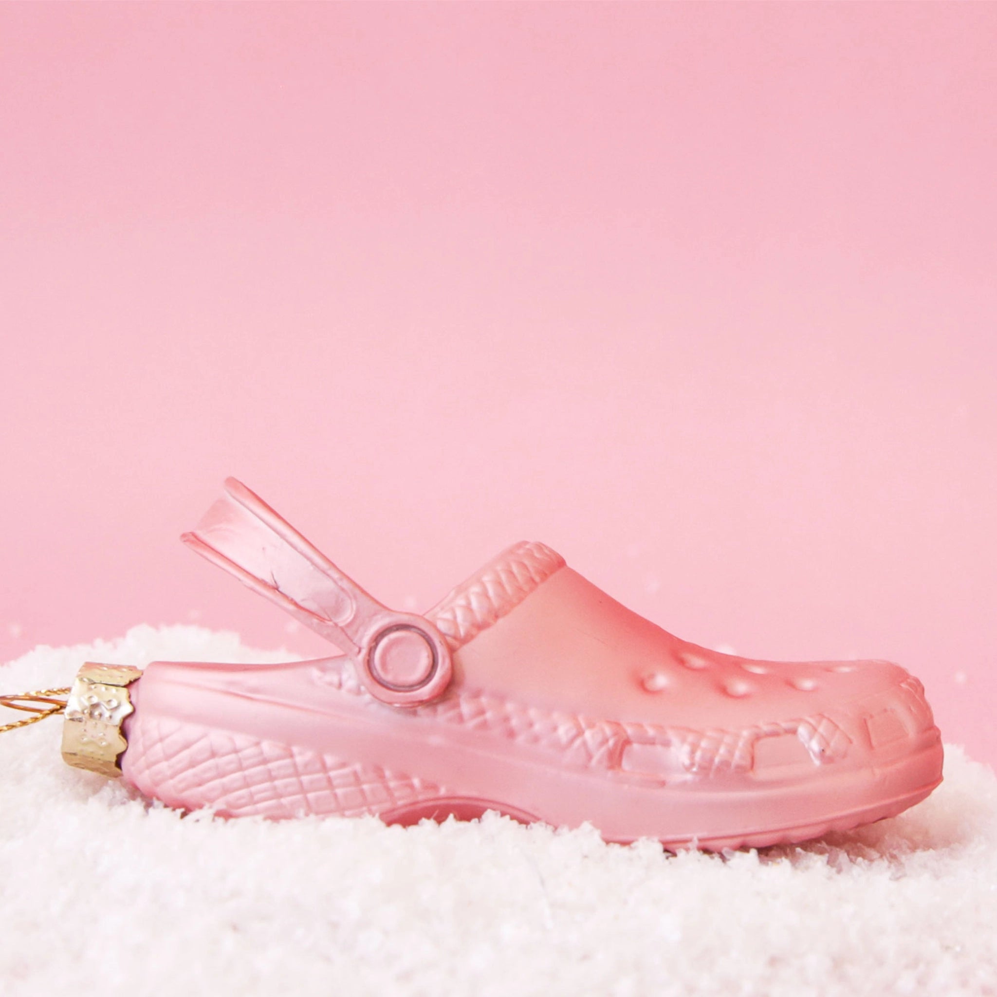 On a pink snowy background is a pink glass ornament in the shape of a clog shoe. 