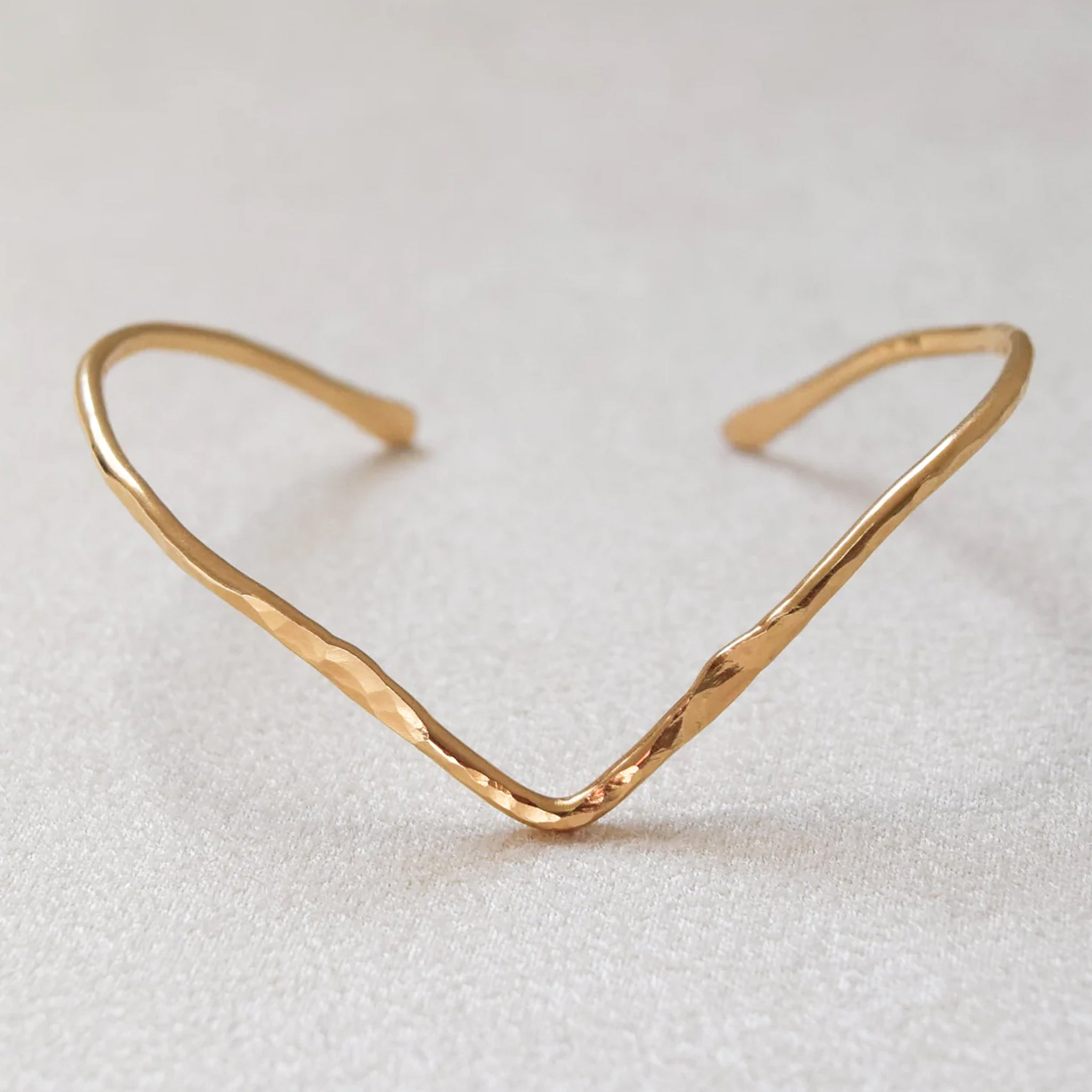 A gold hammered cuff bracelet with a pointed shape. 