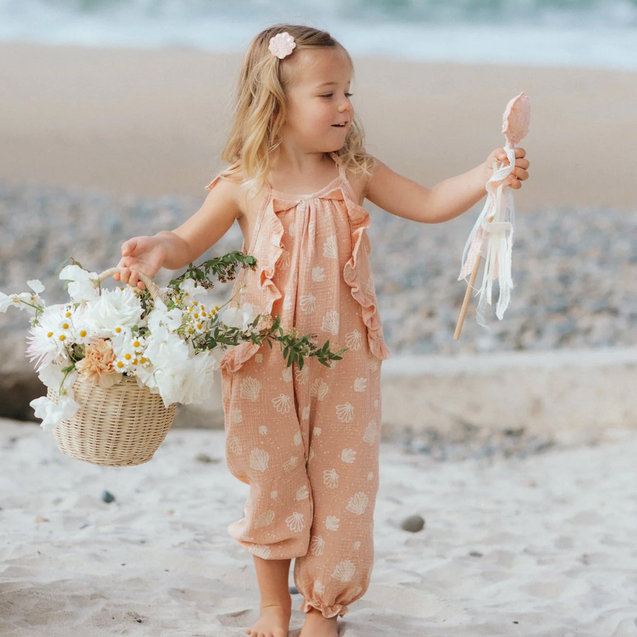 A pink and ivory seashell printed jumpsuit for children with shoulder tie details and a ruffle detail.