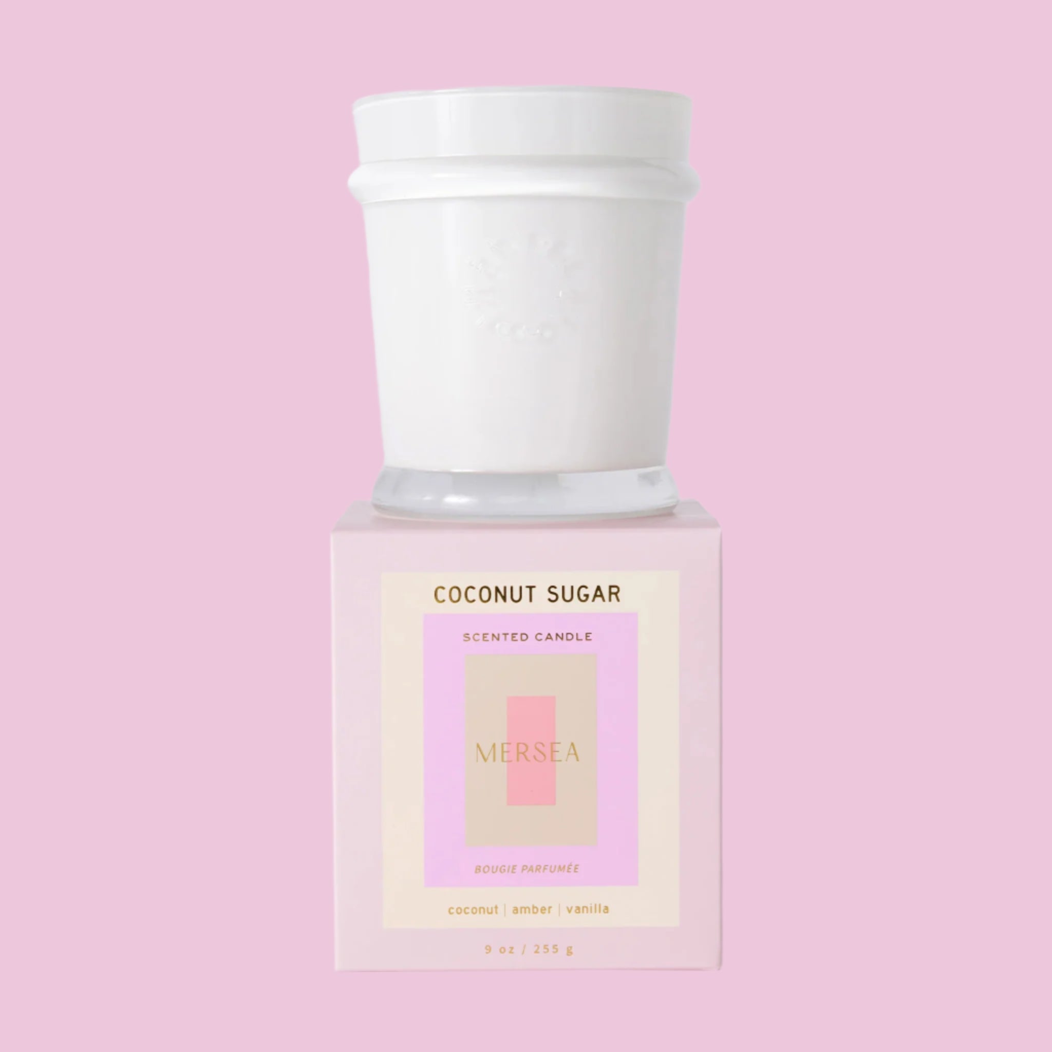 A white candle with a cool toned pink box with text that reads, 'Coconut Sugar Scented Candle'. 