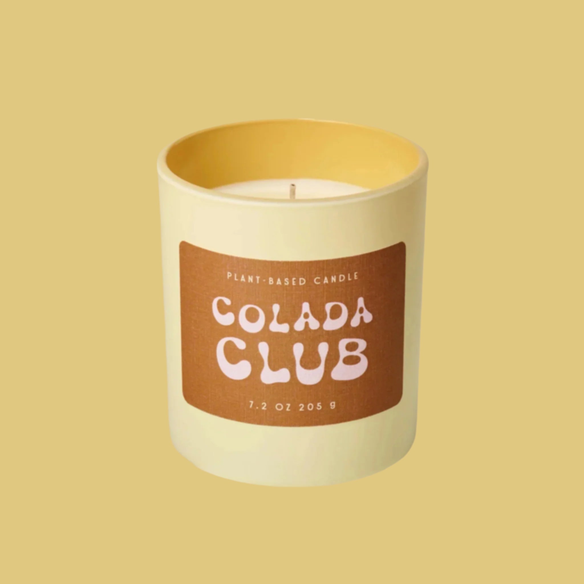 A glass jar candle with a brown label that reads, 'Colada Club'. 