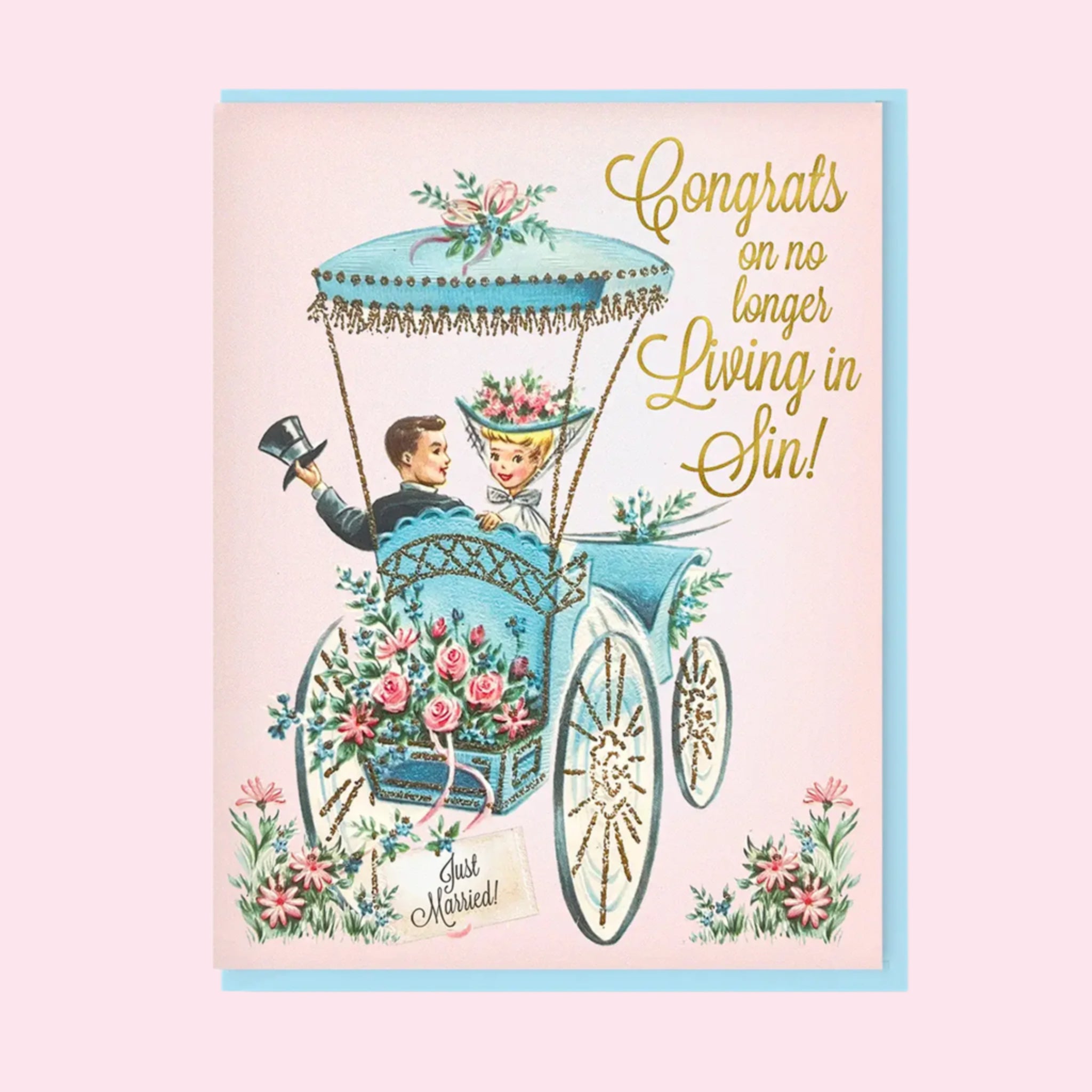 A pink card with a vintage carriage illustration with a newlywed couple paired with a blue envelope and gold foiled text that reads, &#39;Congrats on no longer living in sin!&#39;. 