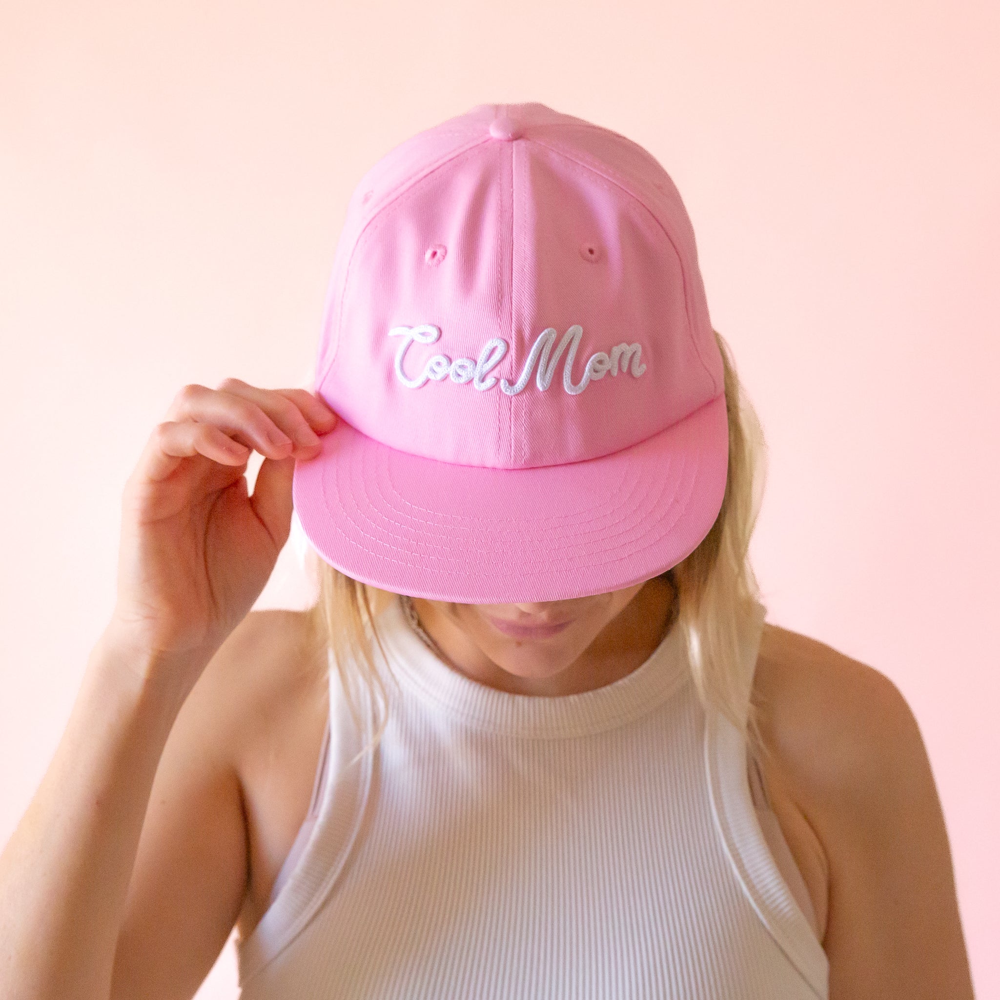 A pink flat brim hat with white embroidered text that reads, 'Cool Mom'. 