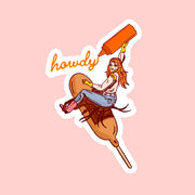 On a pink background is a sticker with a cowgirl riding a corn dog and holding a ketchup bottle that writes "howdy". 