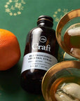 On a green background is a glass bottle of cocktail syrup. 