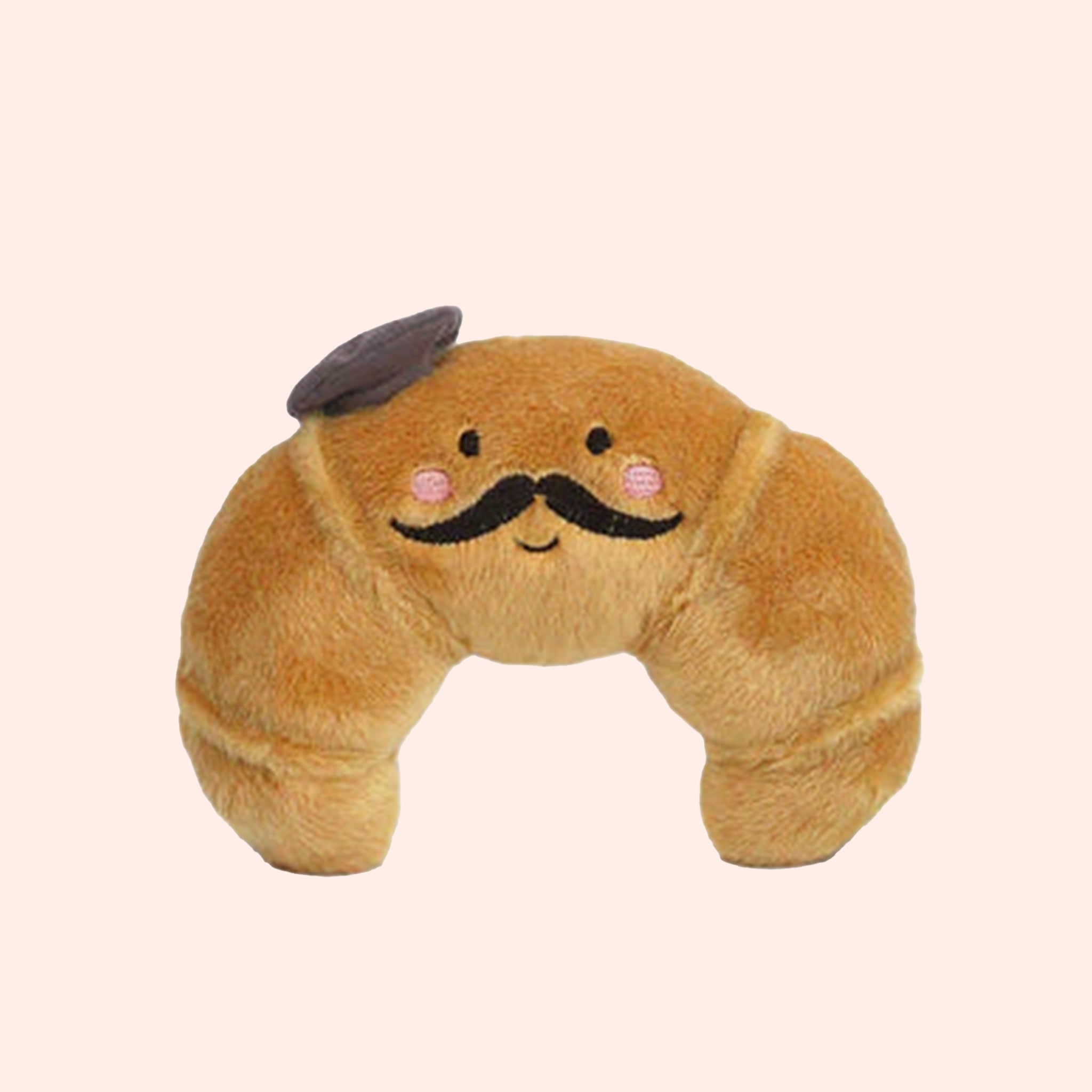 A croissant shaped stuffed toy with a smiling face, a mustache and wearing a French beret. 