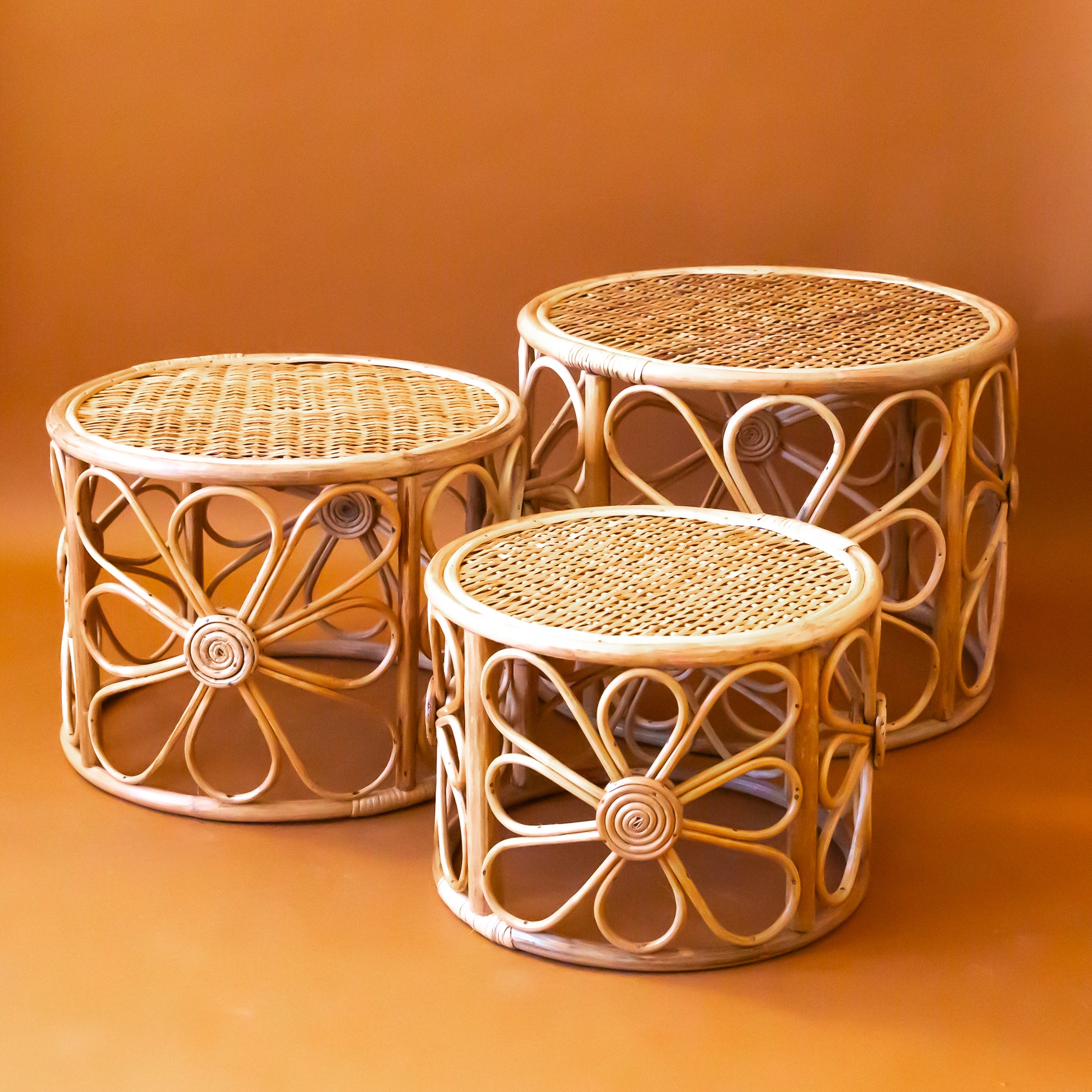 Three rattan nesting tables with a daisy design around the edges.