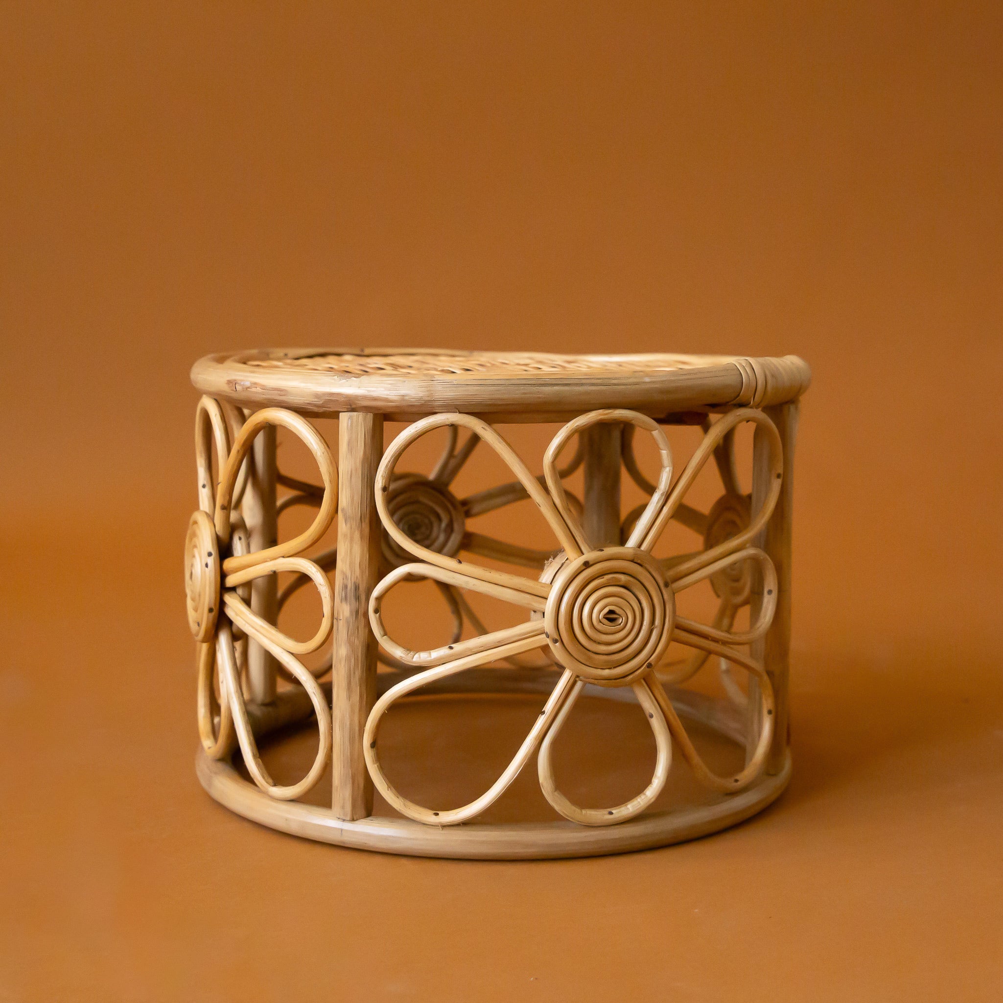 A rattan side table plant stand with a daisy design around the edges. 