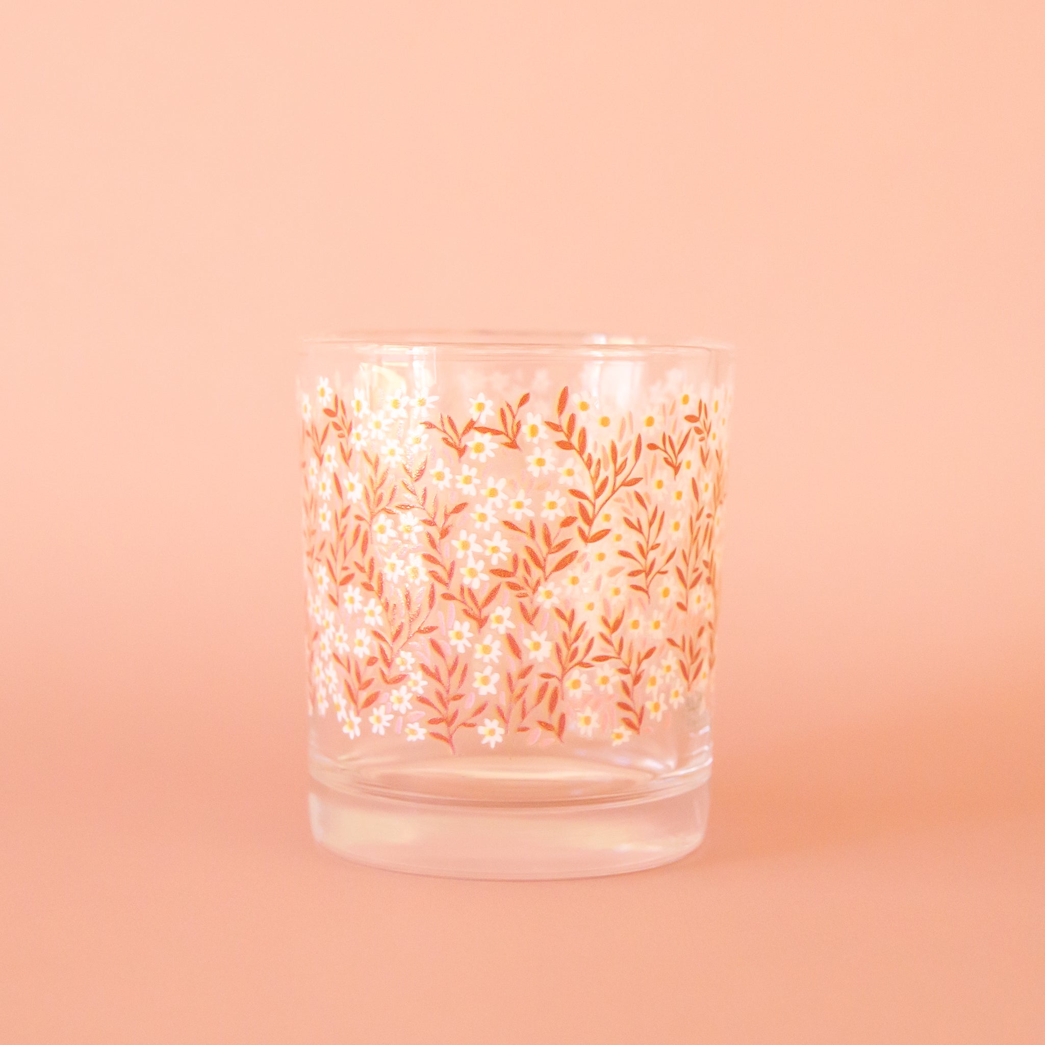 A clear short drinking glass with a pink and white daisy print. 