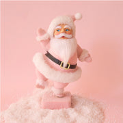 On a pink background is a Santa figurine with a pink flocked suit and white furry details. 