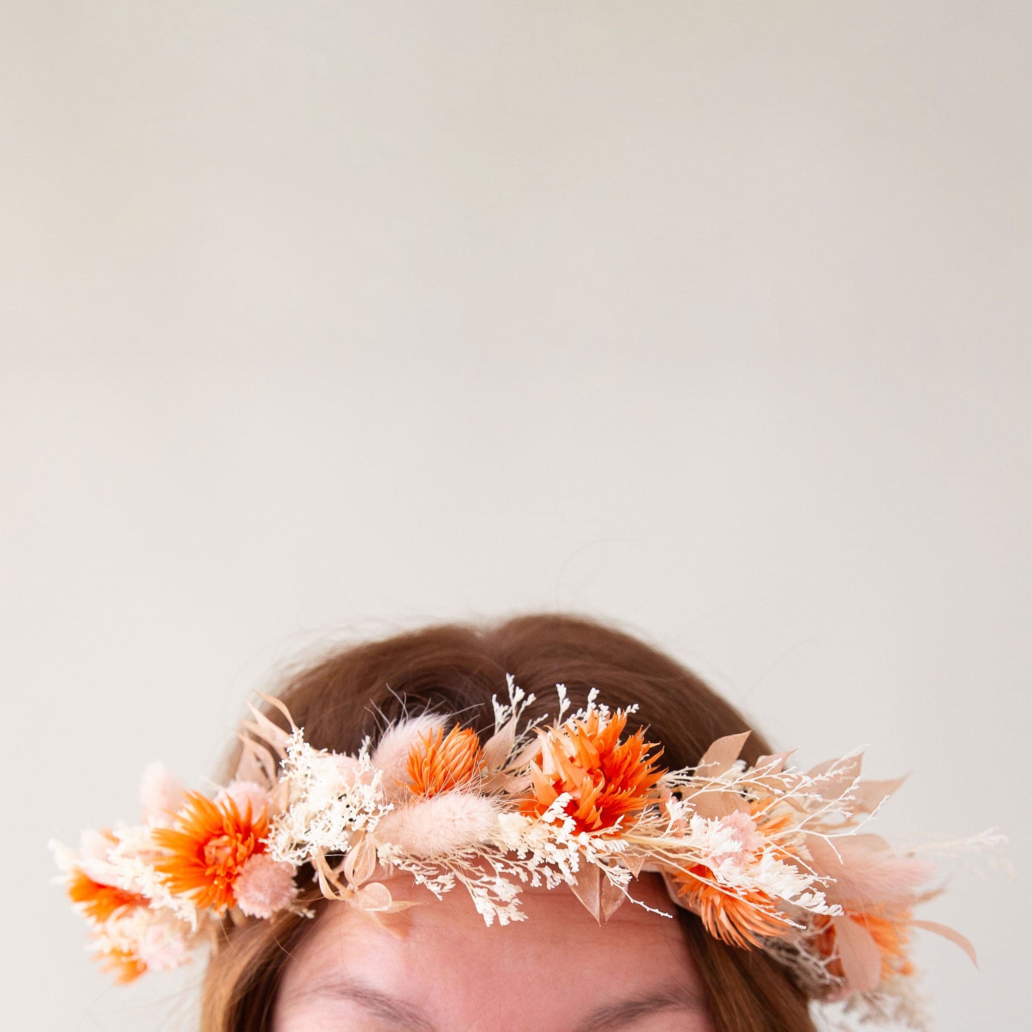 A flower crown made up of orange and neutral dried florals with a ribbon tie detail on the back. 