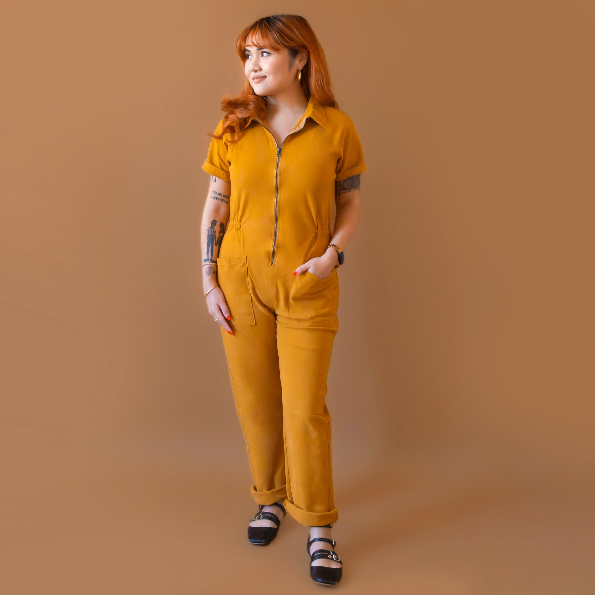 A dijon yellow utility suit with short sleeves, front pockets and a front zipper. 