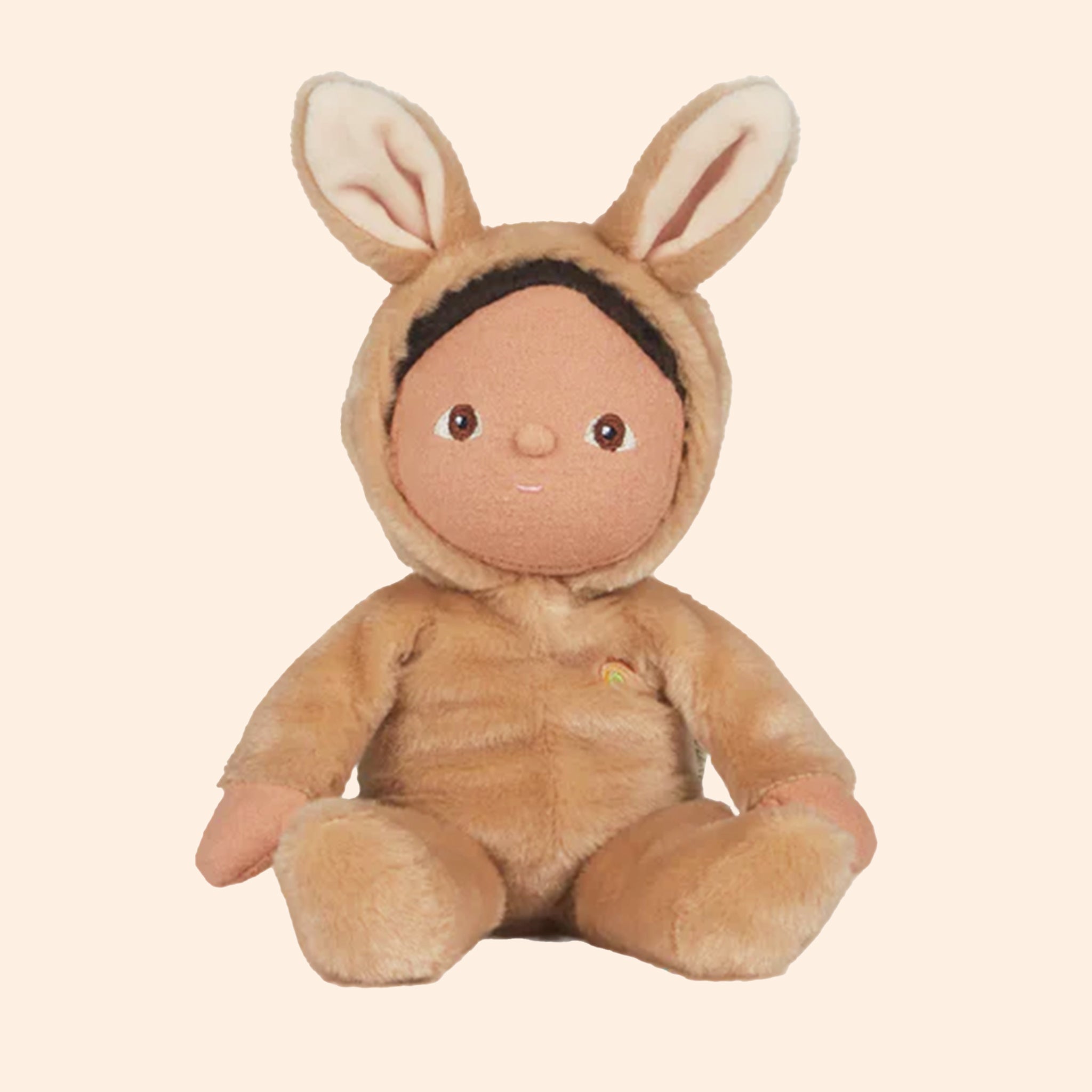 On a tan background is a doll wearing a fuzzy tan bunny onesie.
