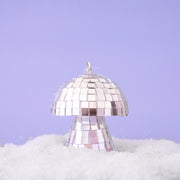 On a purple snowy background is a silver disco mushroom ornament.