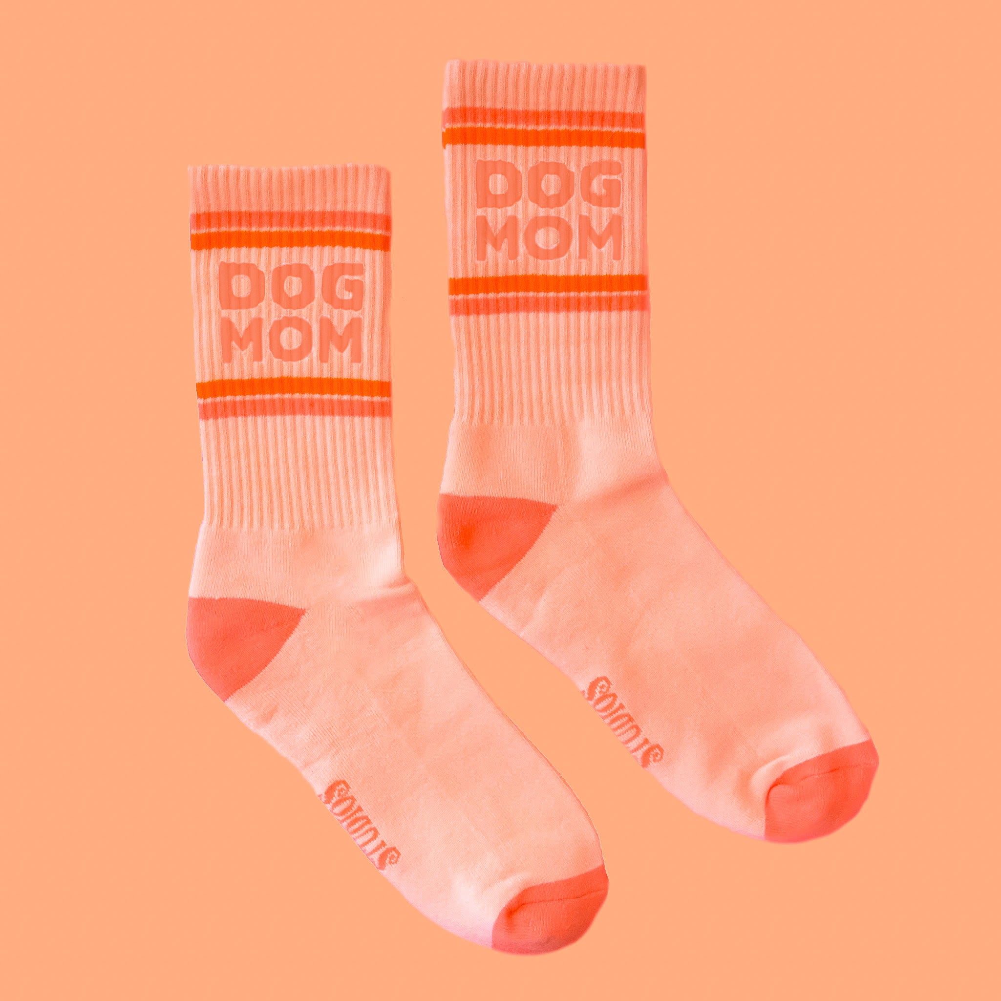 Peachy pink ribbed crew socks with orange text that reads, 'Dog Mom' on the ankle of the socks. 