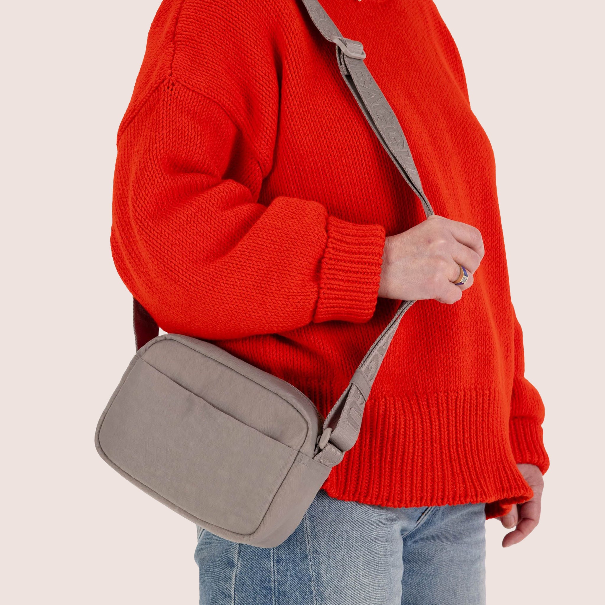 A tannish grey colored crossbody bag with an adjustable strap.