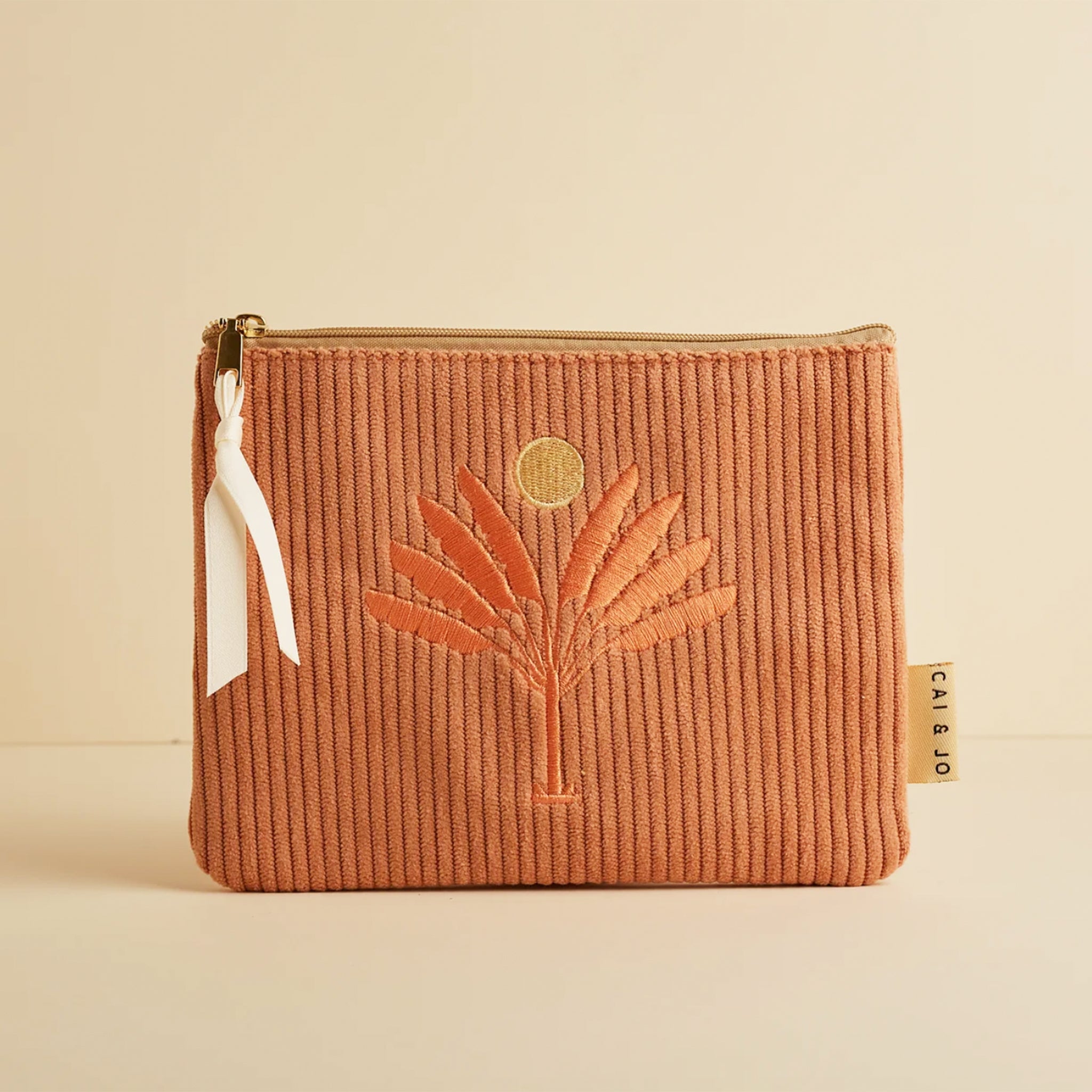 A dusty pinkish orange corduroy pouch with a desert palm and sun design.