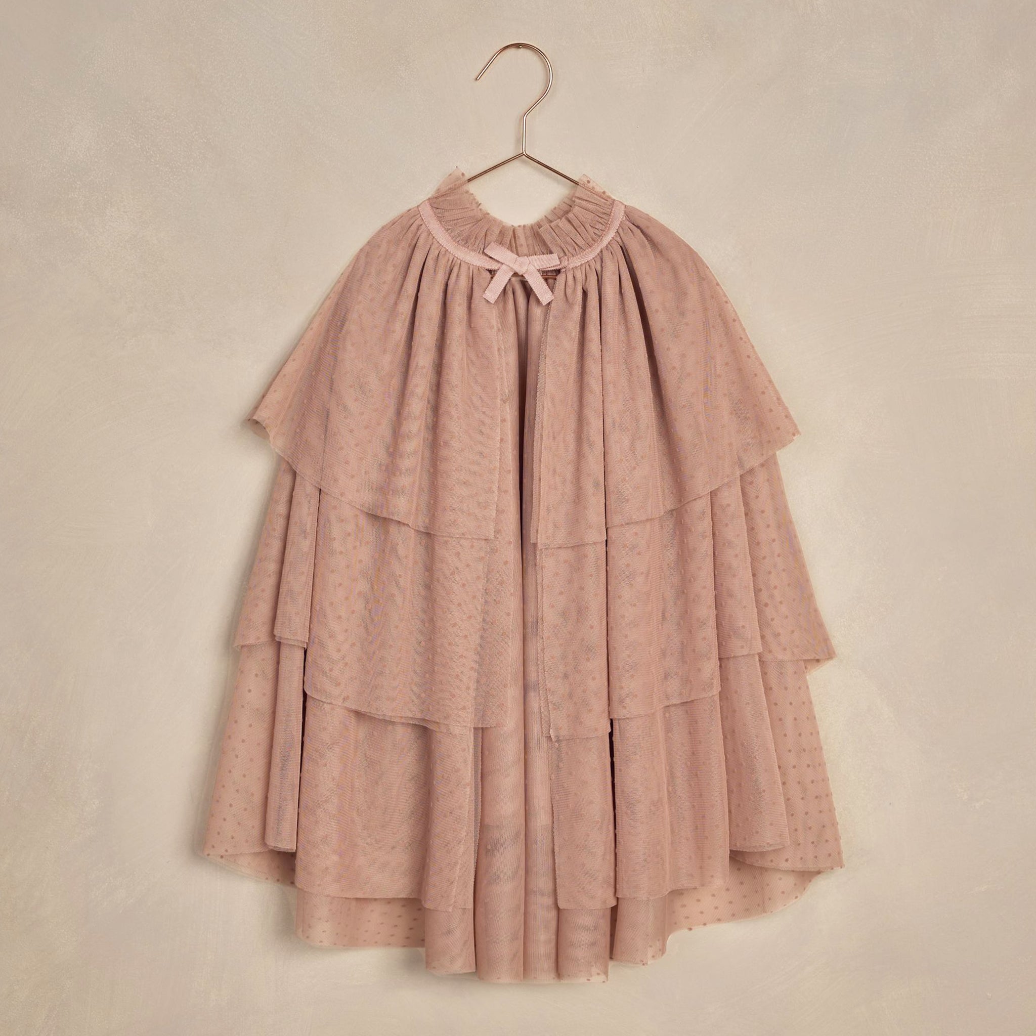 A dusty pink tulle cape with tiered layers and a tie at the neck. 