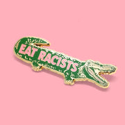 On a pink background is a crocodile shaped pin with text across that reads, "Eat Racists". 