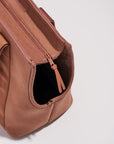 On a white background is a brownish/tan tote bag for carrying pets with two straps and a padded black bottom.