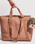 On a white background is a brownish/tan pet carrier tote with a spot for the pet's head to poke out and two straps. 