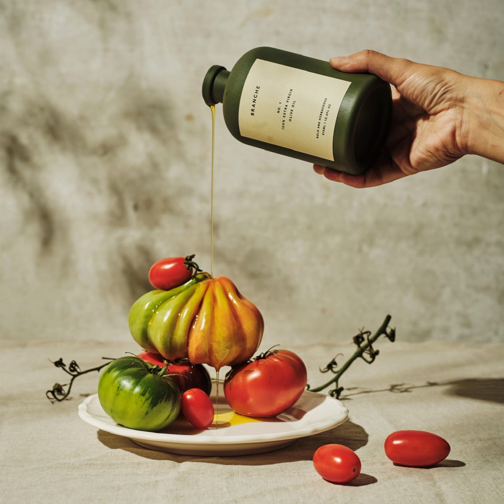 A green bottle of olive oil with a cork lid and an off white label with black text that reads, &#39;Branche No. 1 100% Extra Virgin Olive Oil&#39;. 