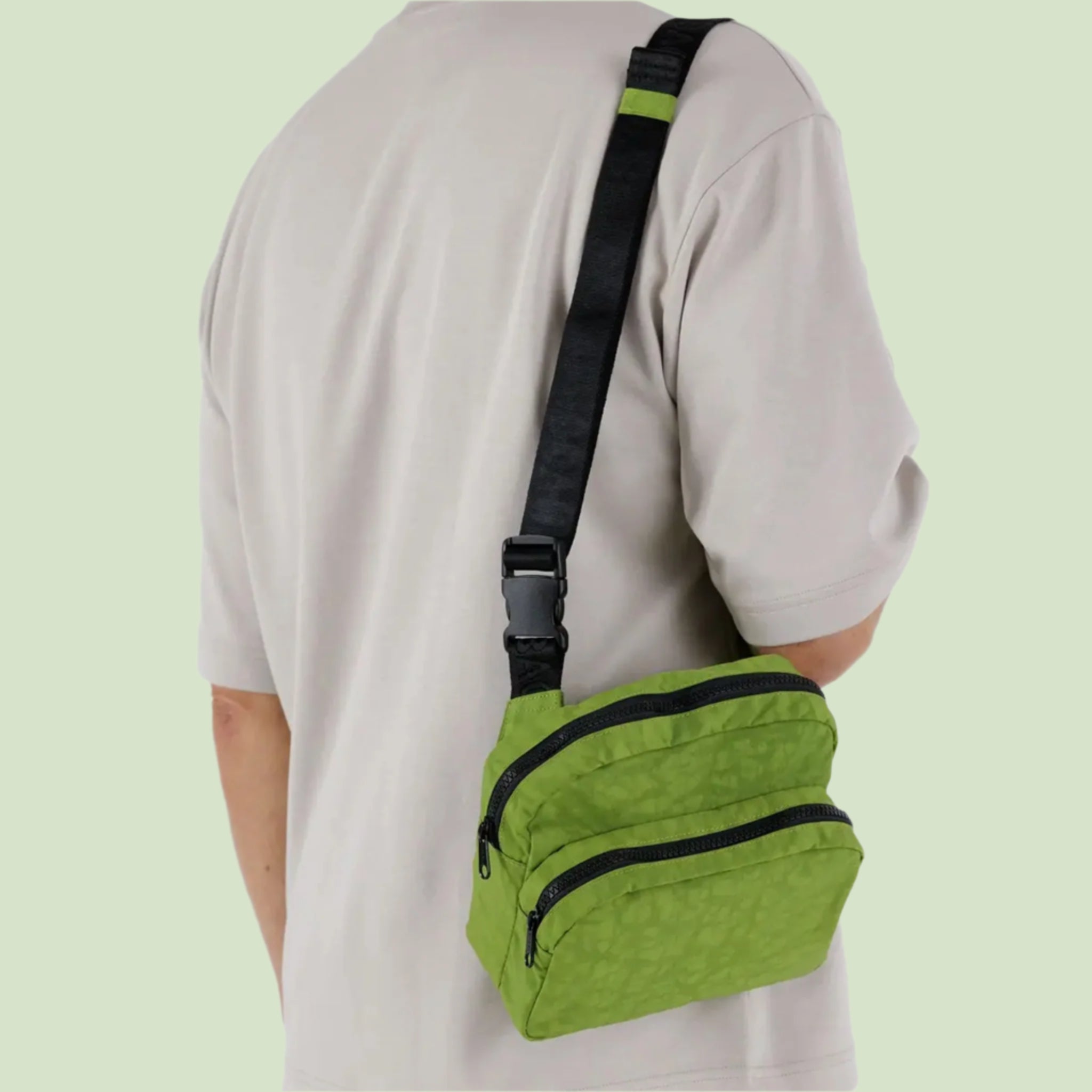 A green fanny pack with a black strap and zipper details. 