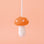 Orange felt mushroom ornament with white spots on the mushroom cap, and a white stem are shown against a peach colored background. 