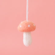 On a pink background is a felt mushroom ornament with a peachy pink top and cream accents. 