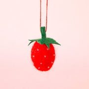 On a pink background is a felt strawberry ornament. 