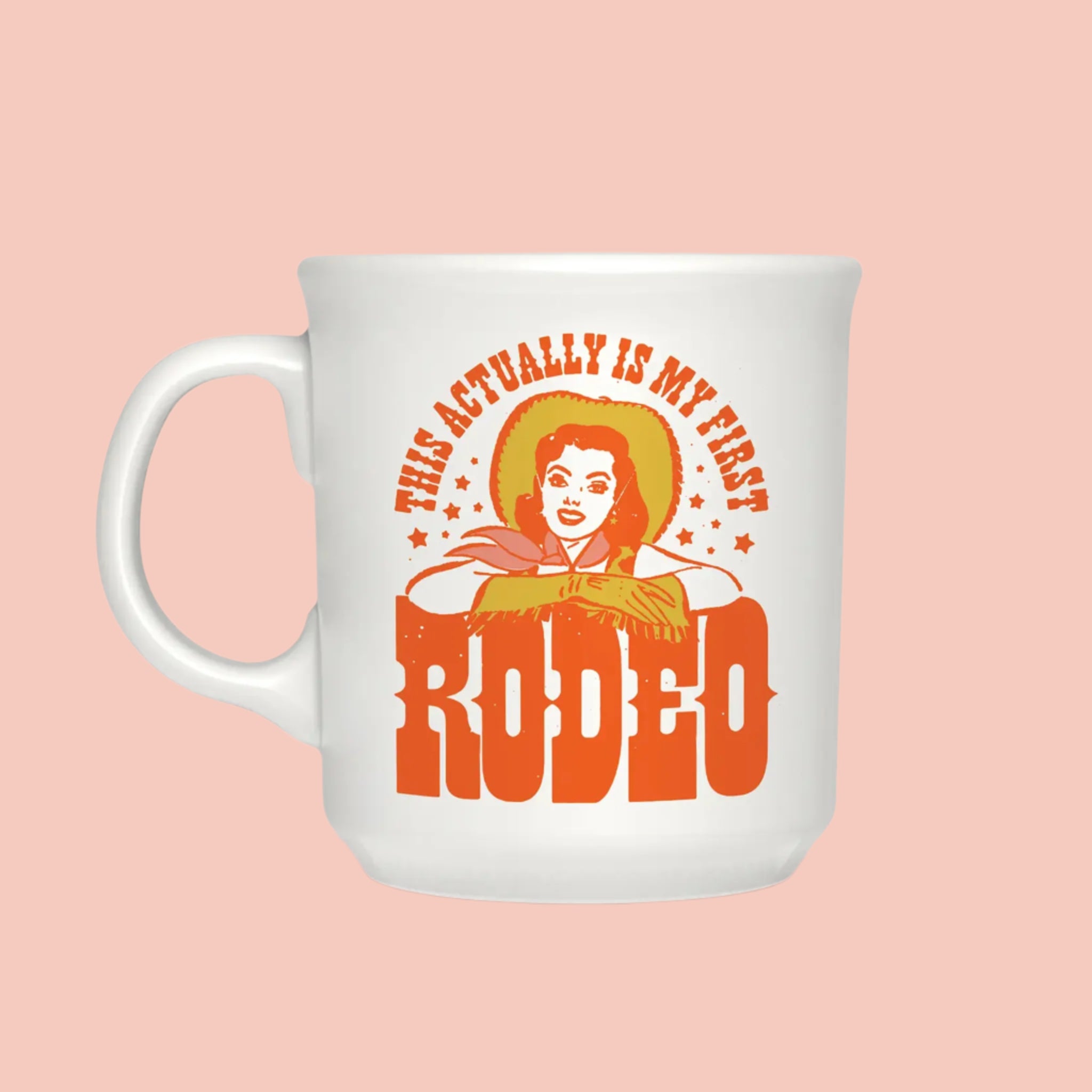 A white mug with a vintage inspired cowgirl graphic leaning over text that reads, 'This Actually Is My First Rodeo'. 