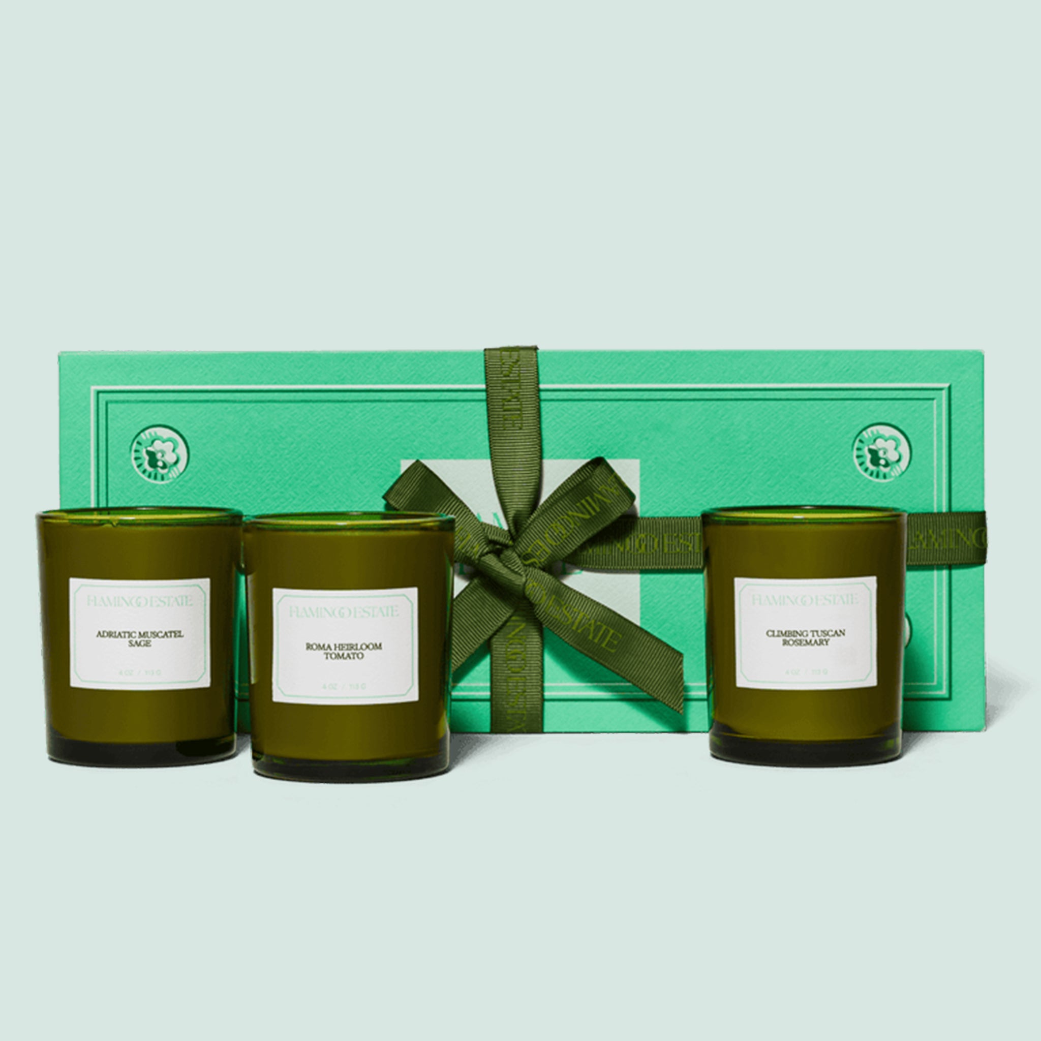 Three green glass jar candles with white labels and in a green gift box. 